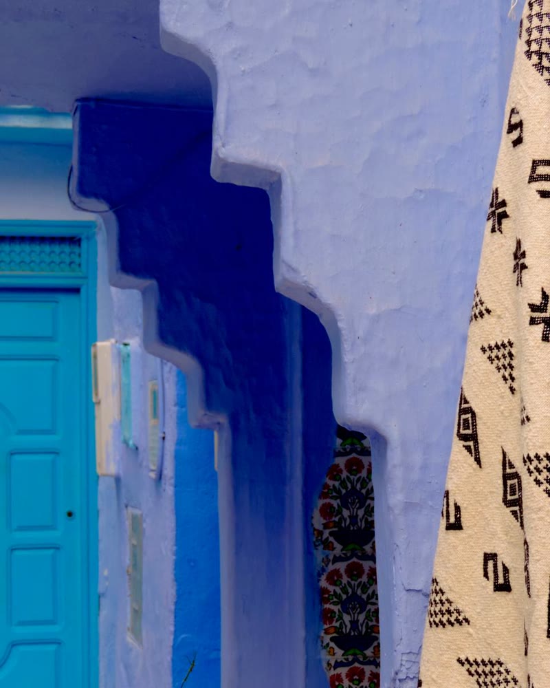 Una porta turchese e un tessuto berbero appeso su un muro blu a Chefchaouen.
