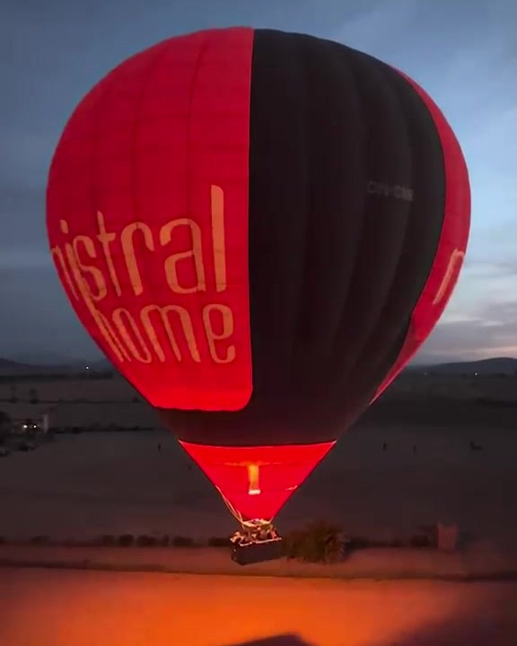 Una mongolfiera all'alba, il bruciatore acceso illumina di rosso il pallone.